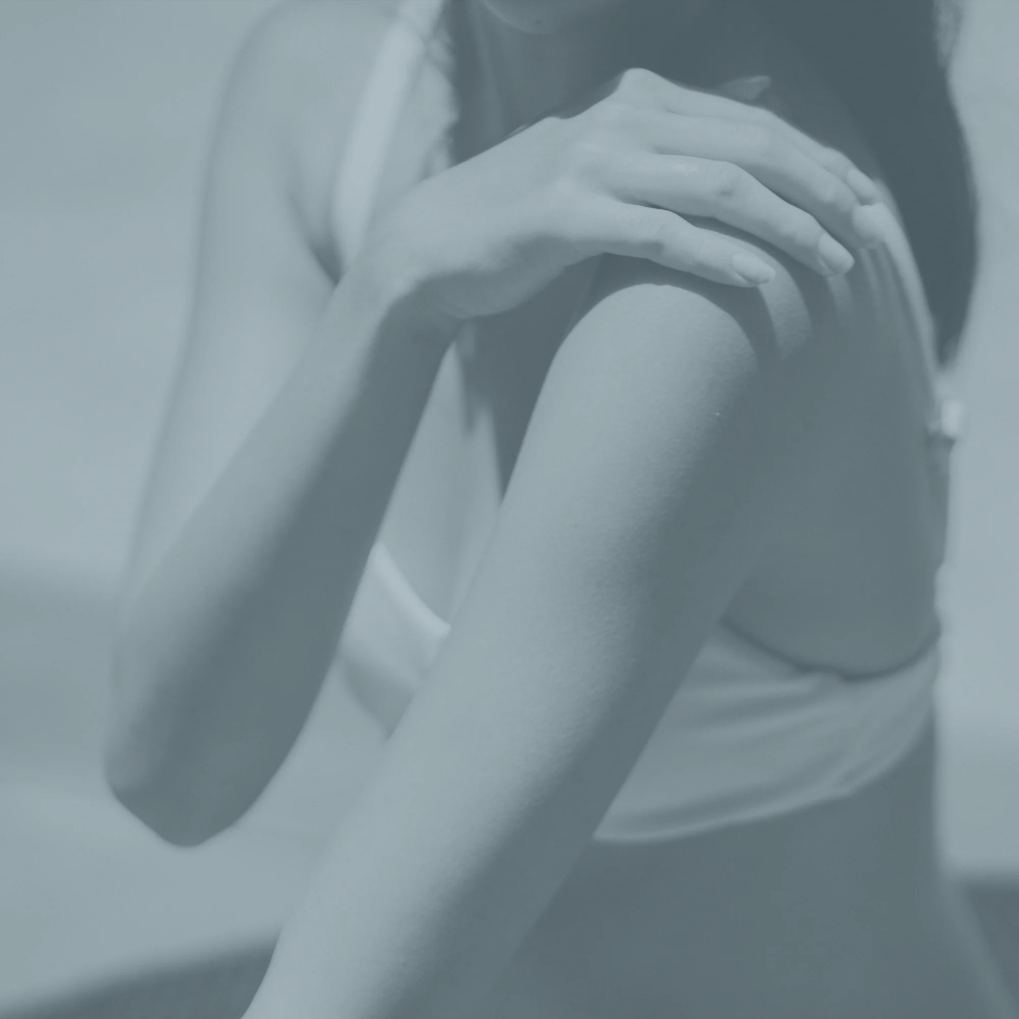 Editorial study of a woman’s shoulder and arm, rendered in the practice’s slate duotone