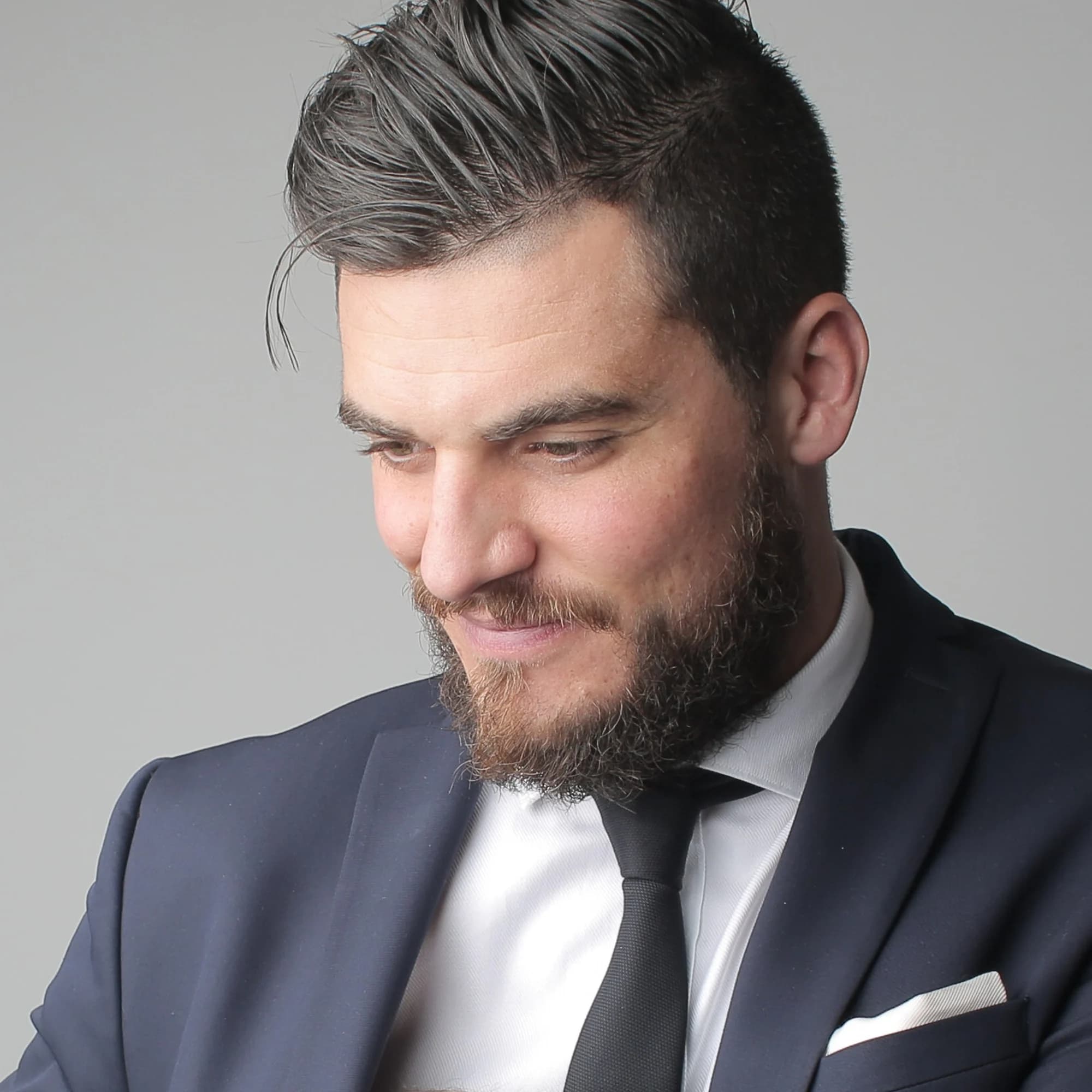 Editorial portrait of a man in a dark suit, photographed against a pale backdrop