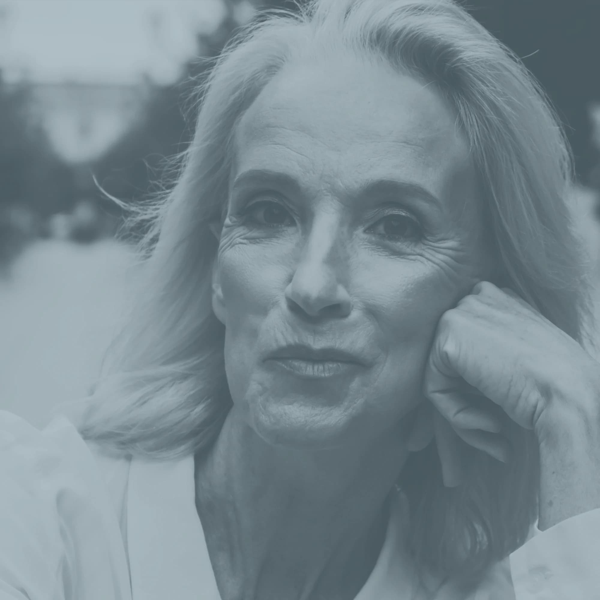Editorial portrait of an older woman resting her cheek on her hand, rendered in the practice's slate duotone