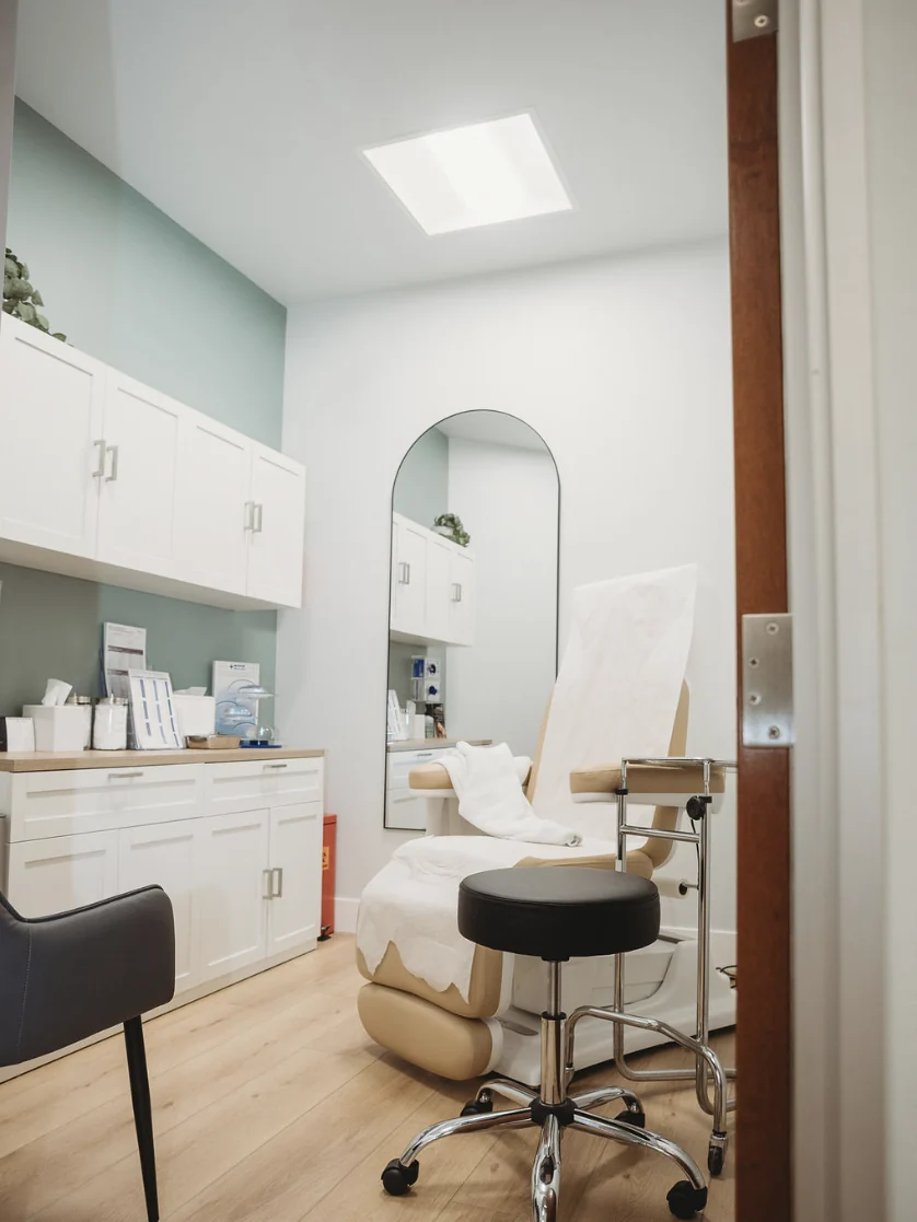 A treatment room at Mafi Plastic Surgery with a reclining facial chair, an arched mirror and cabinets of supplies