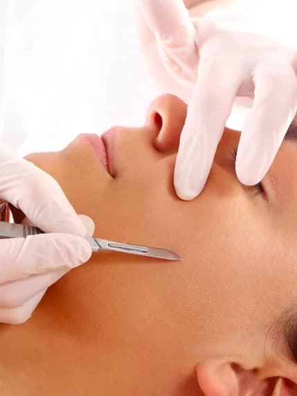 A gloved esthetician drawing a blade across the cheek of a reclined client